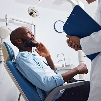 Patient in treatment chair smiling at dentist holding clipboard