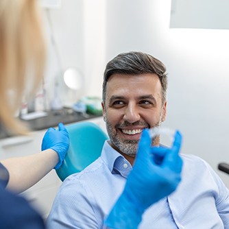 a smiling man looking at a dental assistant as she shows him Invisalign aligners