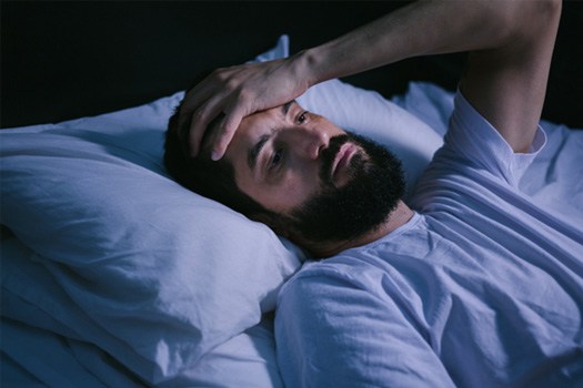 Man in bed awake holding hand to forehead