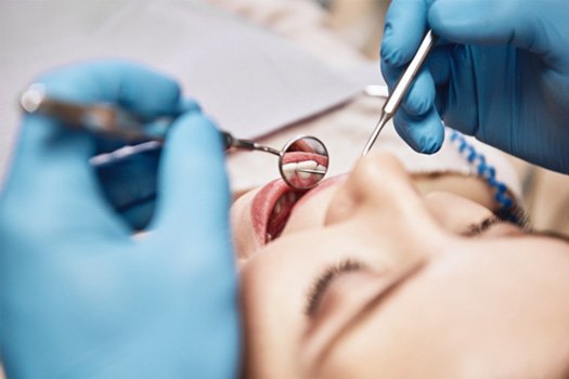 Gloved hands holding dental instruments reflecting woman’s teeth