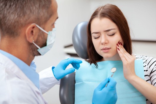 Woman in dental chair with eyes closed holding hand to jaw in pain