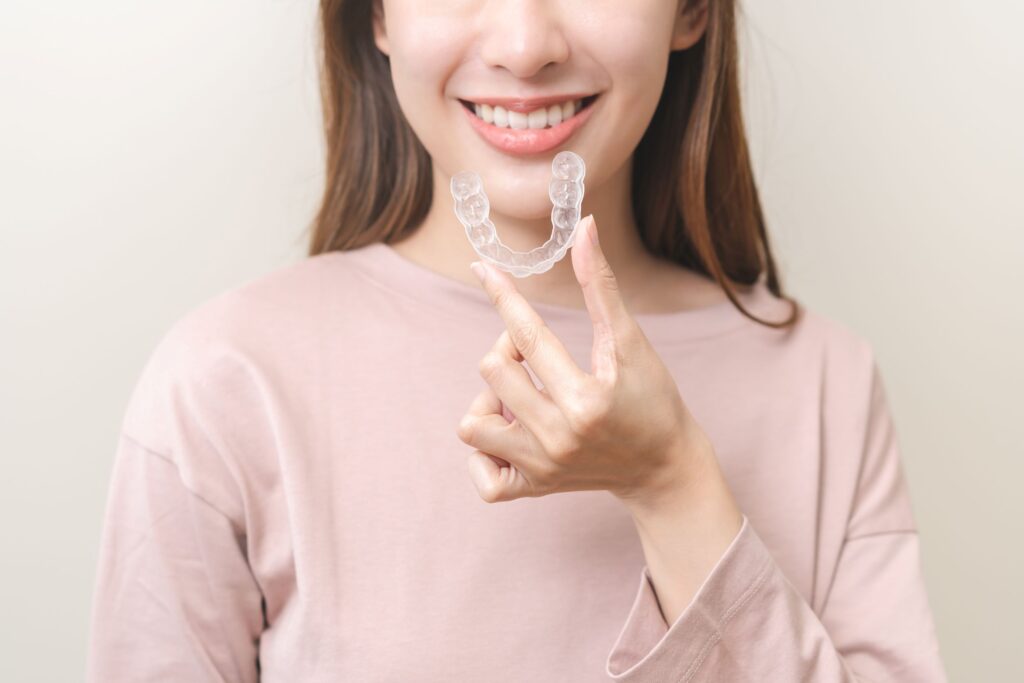Woman in beige shirt holding Invisalign to her teeth