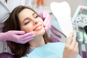 Woman smiling at reflection in mirror with dentist touching her cheeks